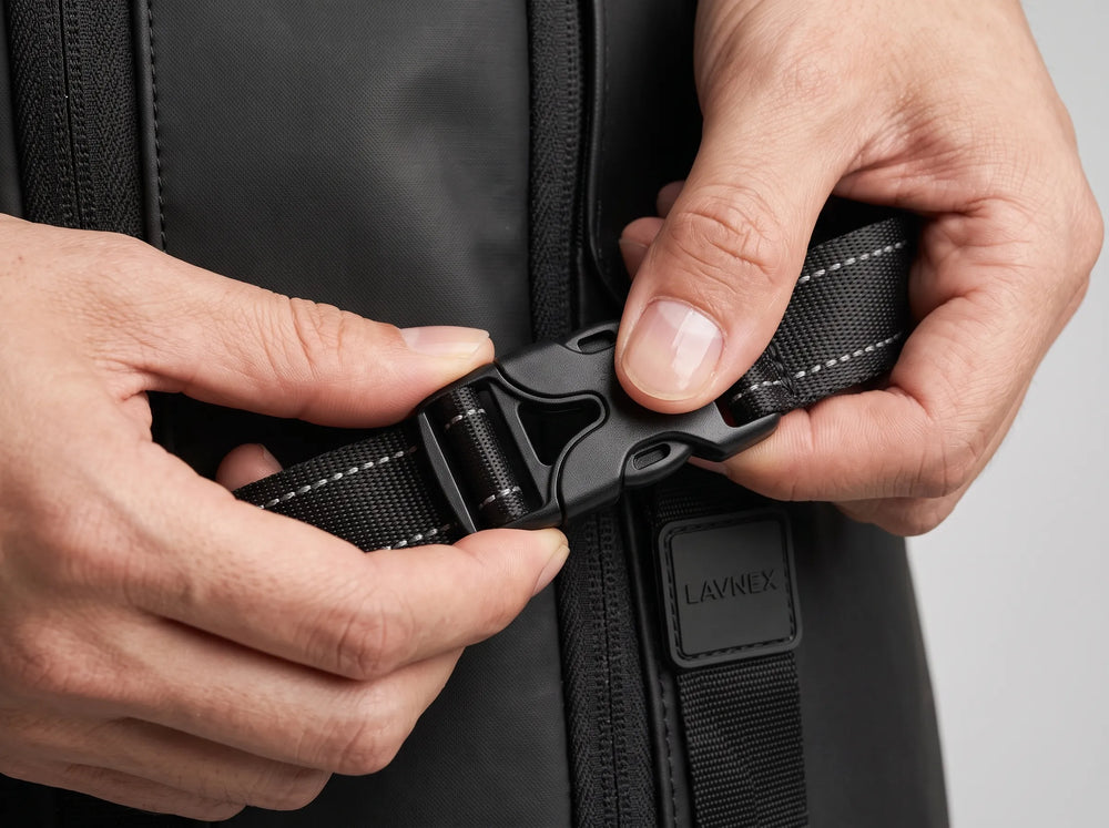 Close‑up of hands fastening black buckle on Lavnex ZoraPack Pro™ Jet Black backpack showing durable strap and precise stitching