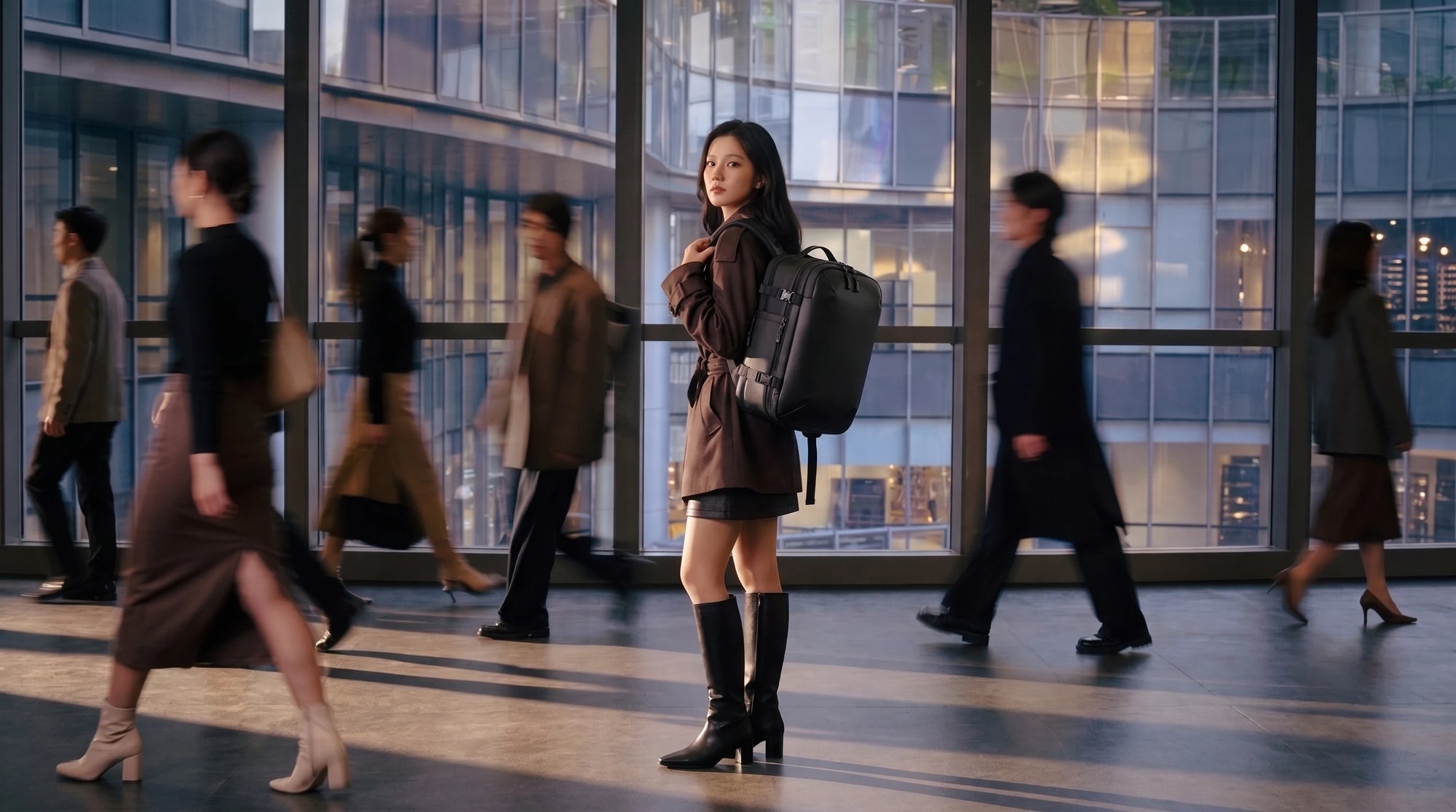 Woman standing confidently in modern city walkway carrying Lavnex ZoraPack Pro™ Jet Black backpack while people move around her in motion blur