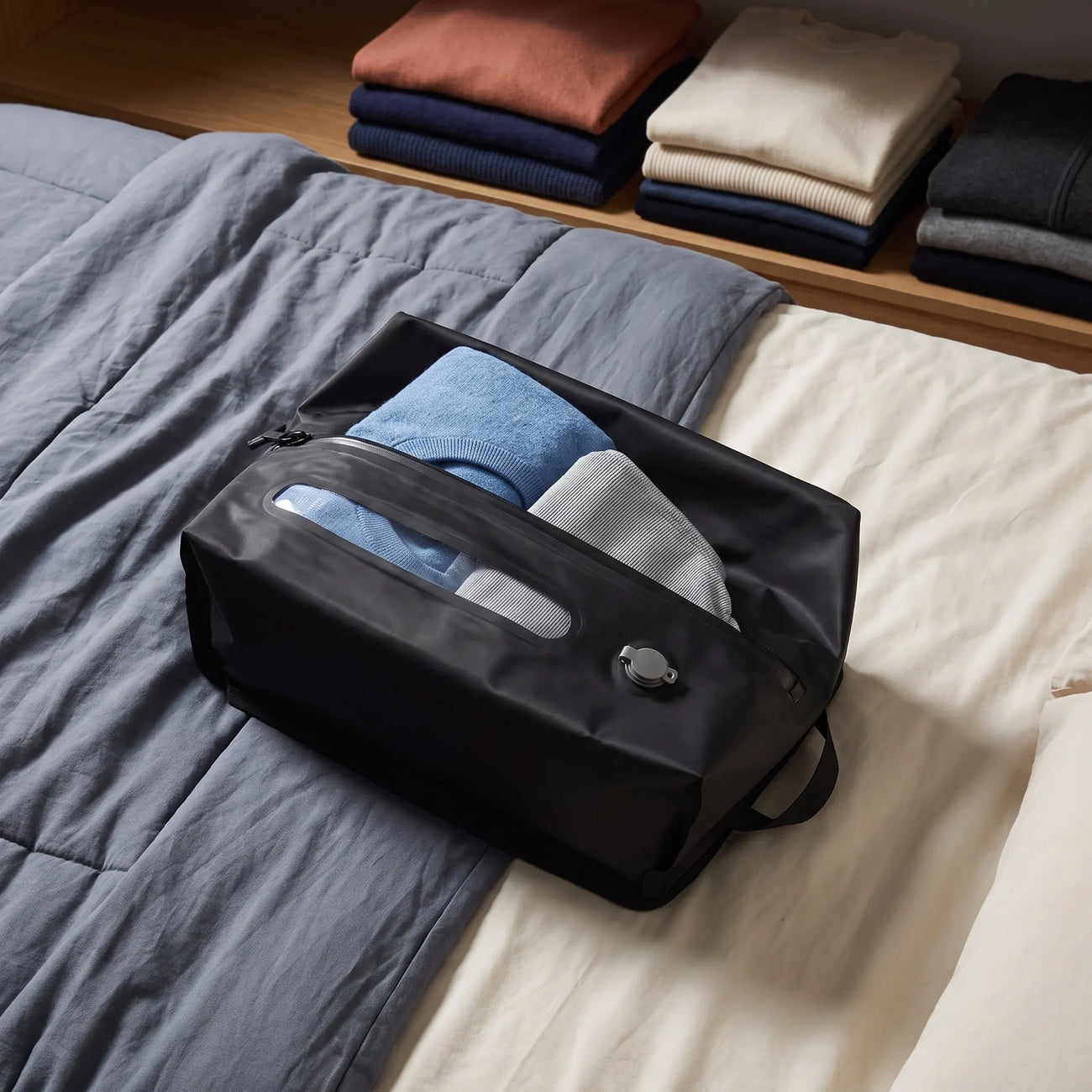 Lavnex Still Vac™ Jet Black vacuum compression bag placed on bed with folded clothes inside and organized wardrobe in background