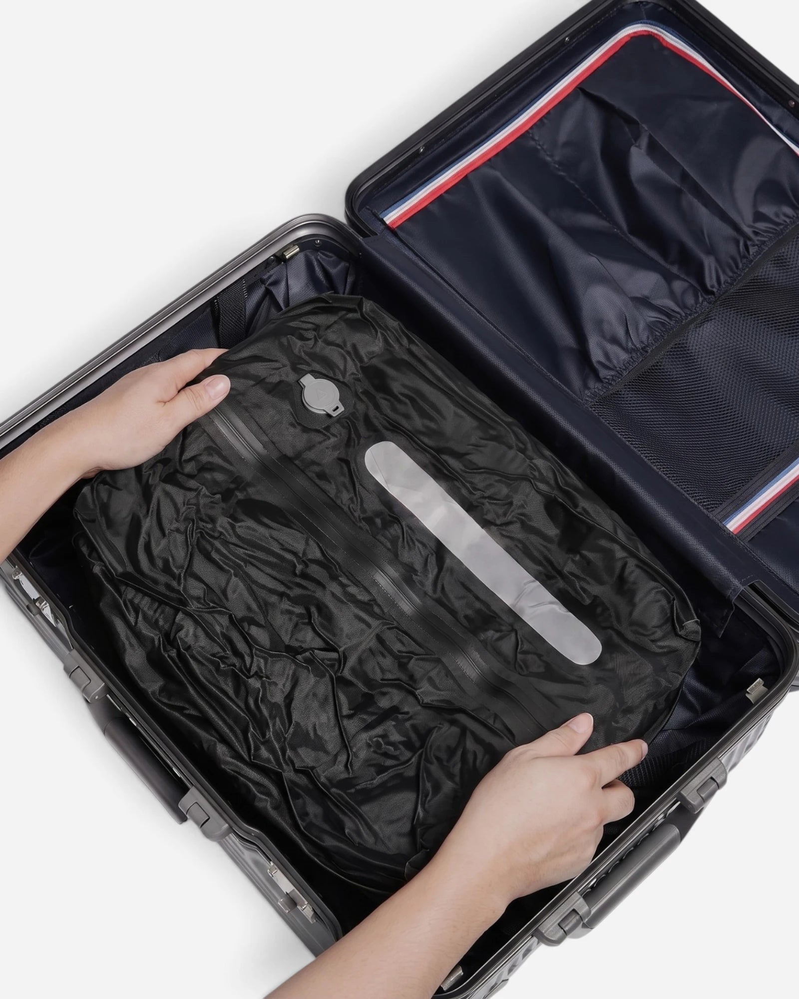 Hands placing Lavnex Still Vac™ Jet Black vacuum compression bag inside open suitcase with dark lining and mesh divider