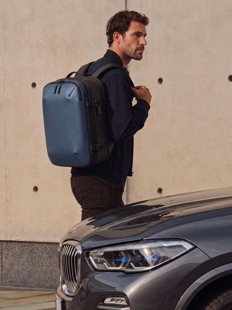 Man carrying Lavnex ZoraPack Pro™ Midnight Navy backpack standing beside luxury car in modern city setting