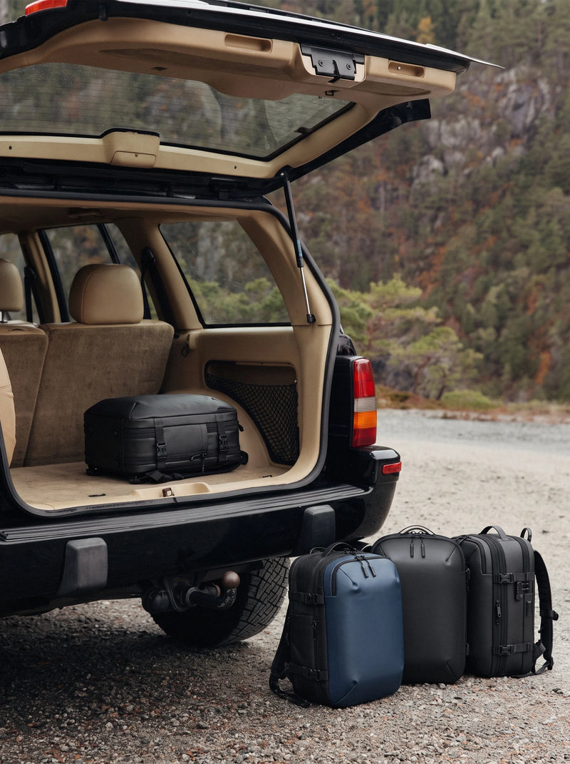 Open SUV trunk with Lavnex ZoraPack Pro™ backpacks in Jet Black and Midnight Navy colors placed on gravel road near forest landscape
